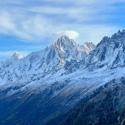 Snow-dusted granite spires rising above a forested valley under a blue sky